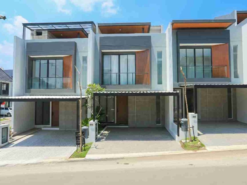 Row of three modern gray townhouses with large glass windows and covered driveways on a sunny street.