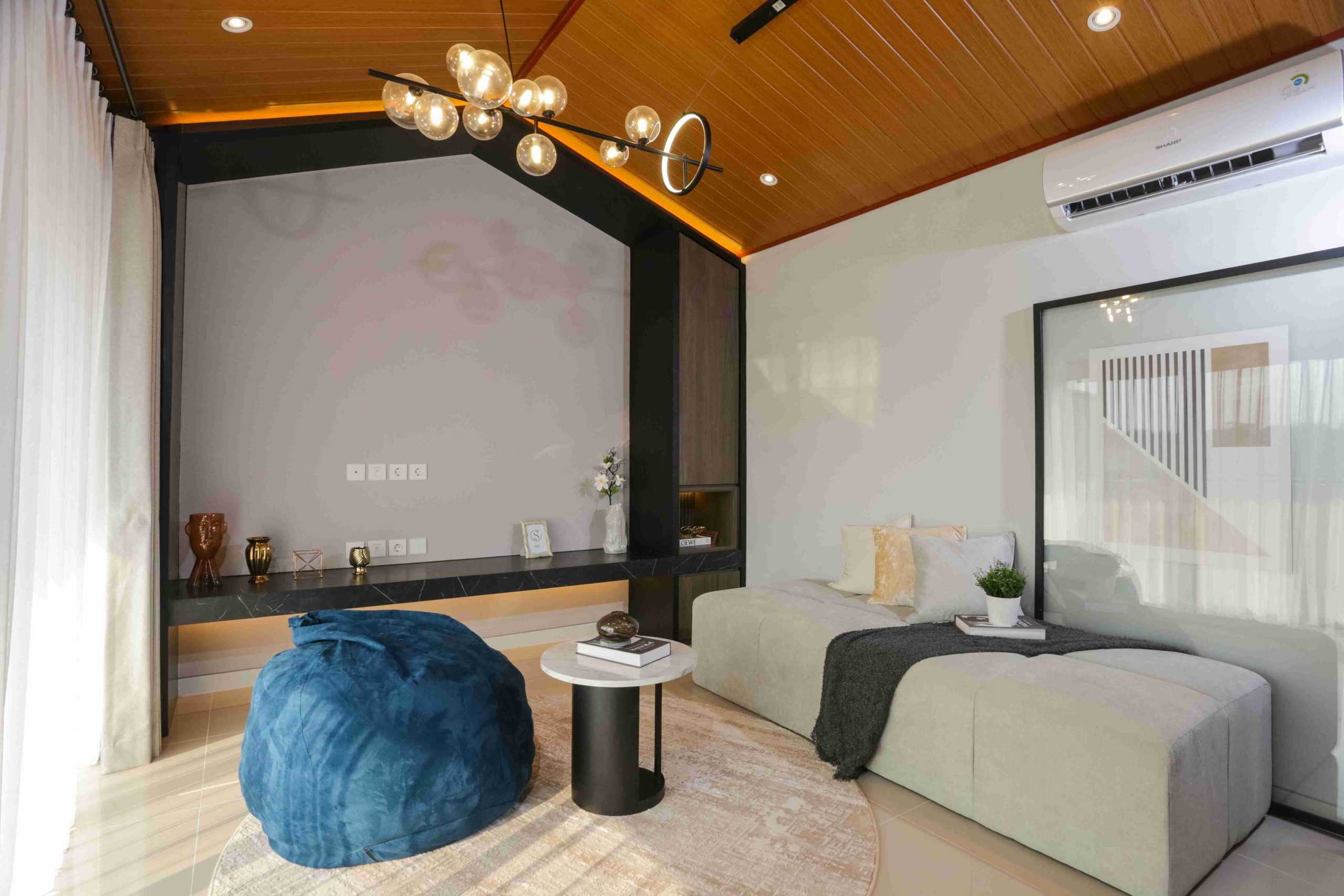 Contemporary living room with beige sectional sofa, a blue pouf, round white coffee table, and glass partition wall paneling.